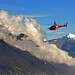 A helicopter flying among the clouds above the snow-capped mountains
